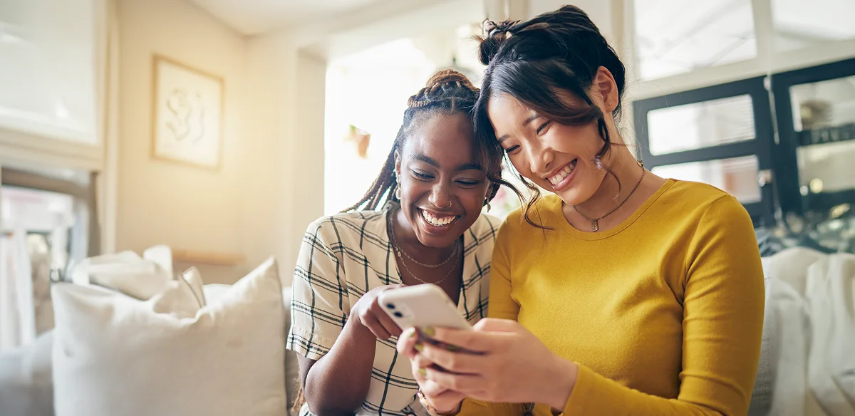 Two students smiling while looking at their cellphone